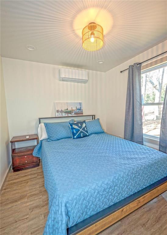 bedroom with a wall unit AC, wood finished floors, and baseboards
