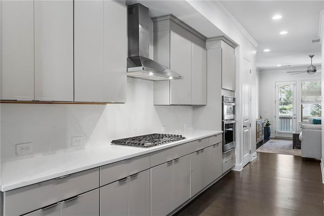 kitchen with ornamental molding, wall chimney range hood, gray cabinets, stainless steel appliances, and dark hardwood / wood-style floors