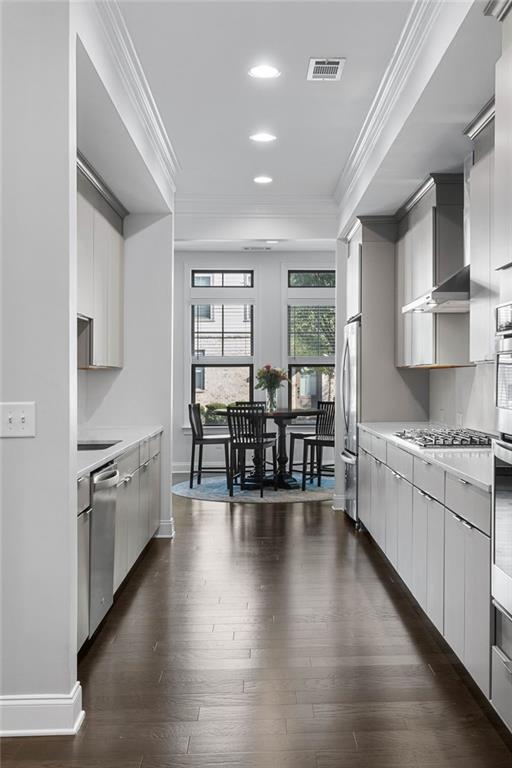 kitchen featuring ornamental molding, stainless steel appliances, wall chimney range hood, and dark wood-type flooring