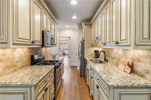 kitchen with cream cabinetry, appliances with stainless steel finishes, light stone countertops, and sink