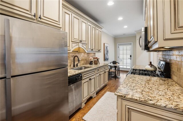 kitchen with sink, light stone counters, cream cabinetry, appliances with stainless steel finishes, and ornamental molding