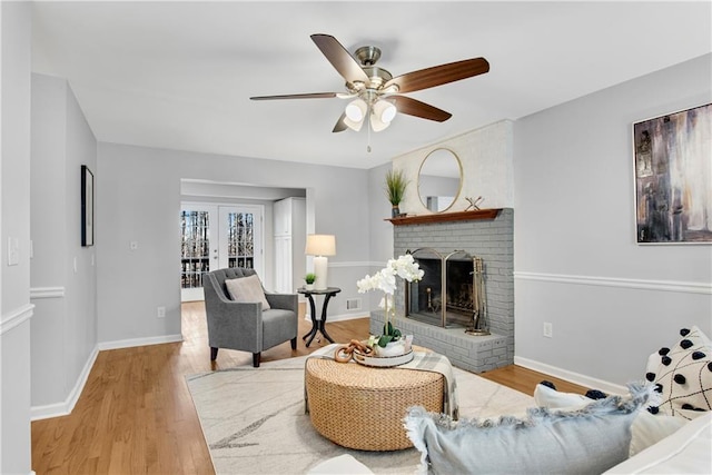 living area with wood finished floors, french doors, baseboards, a brick fireplace, and ceiling fan