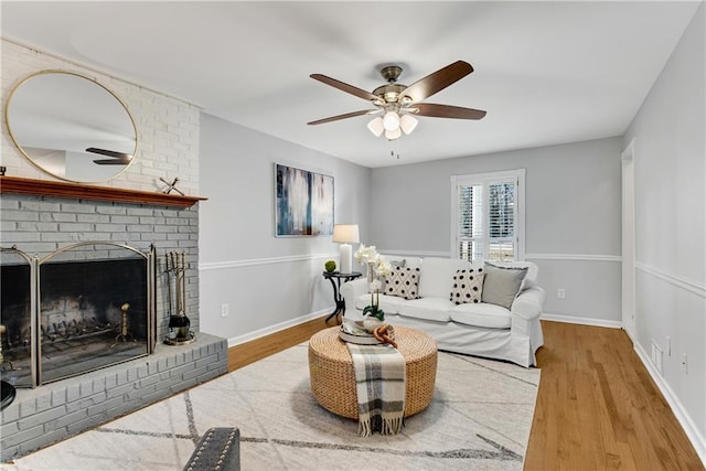 living room featuring a brick fireplace, a ceiling fan, baseboards, and wood finished floors