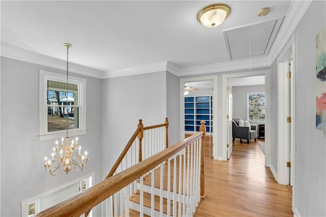 corridor with an upstairs landing, light wood finished floors, attic access, and ornamental molding