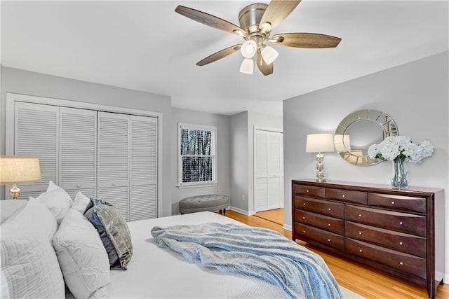 bedroom featuring a ceiling fan, wood finished floors, baseboards, and two closets