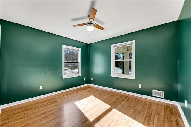 empty room featuring ceiling fan, wood finished floors, visible vents, and baseboards