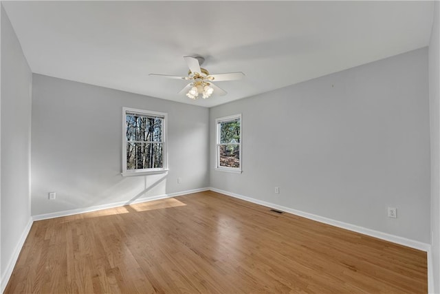 spare room with a ceiling fan, visible vents, wood finished floors, and baseboards