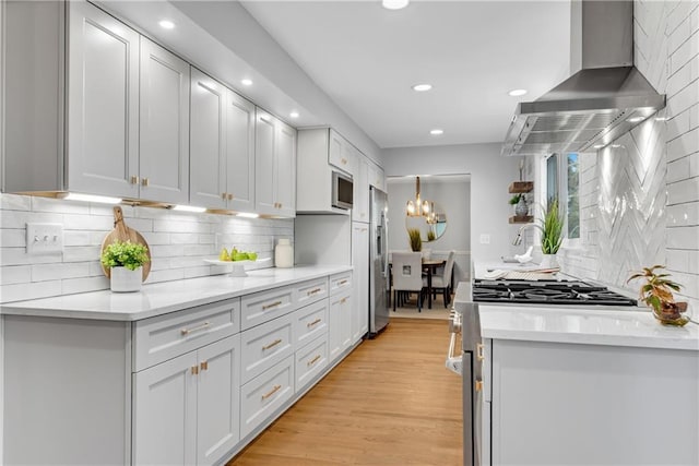 kitchen with recessed lighting, decorative backsplash, appliances with stainless steel finishes, wall chimney range hood, and light wood-type flooring