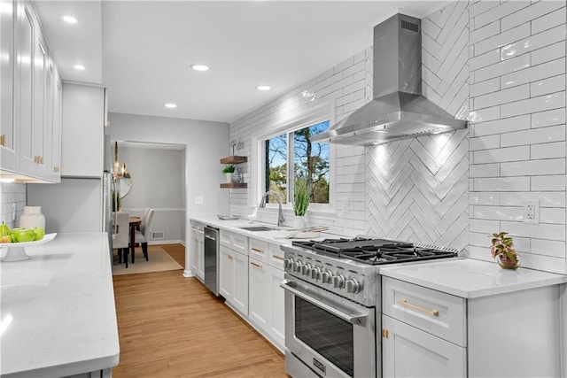 kitchen featuring light wood-type flooring, a sink, appliances with stainless steel finishes, wall chimney exhaust hood, and white cabinets