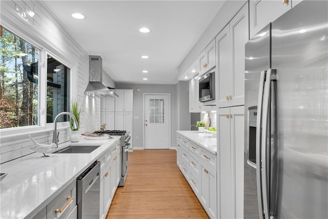 kitchen featuring wall chimney range hood, light wood-type flooring, recessed lighting, stainless steel appliances, and a sink