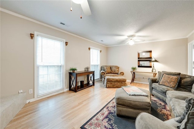 living area featuring crown molding, visible vents, light wood-style flooring, ceiling fan, and a textured ceiling