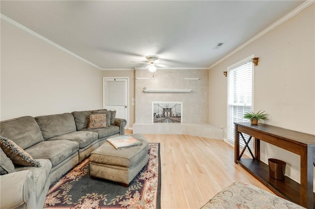 living room featuring visible vents, ceiling fan, wood finished floors, crown molding, and a fireplace