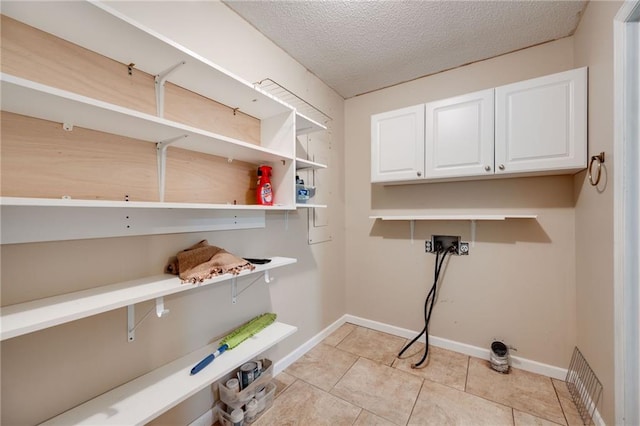 laundry area featuring a textured ceiling, light tile patterned floors, hookup for a washing machine, baseboards, and cabinet space