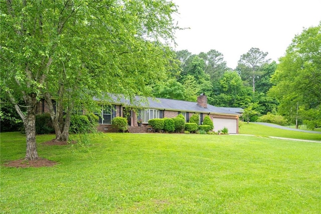 single story home featuring a garage, brick siding, a chimney, and a front yard