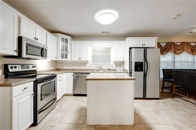 kitchen with appliances with stainless steel finishes, light countertops, white cabinets, and glass insert cabinets