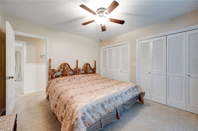 bedroom with a textured ceiling, a ceiling fan, two closets, and light colored carpet