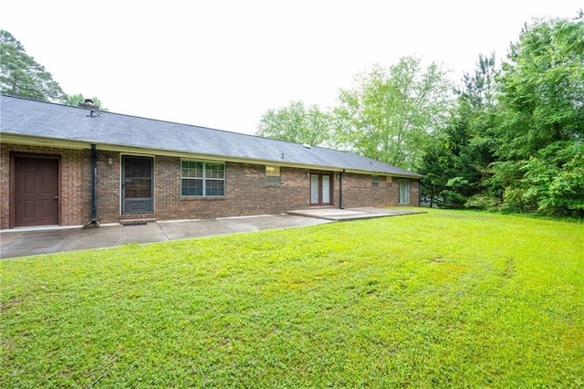 rear view of property featuring a patio area, a yard, and brick siding