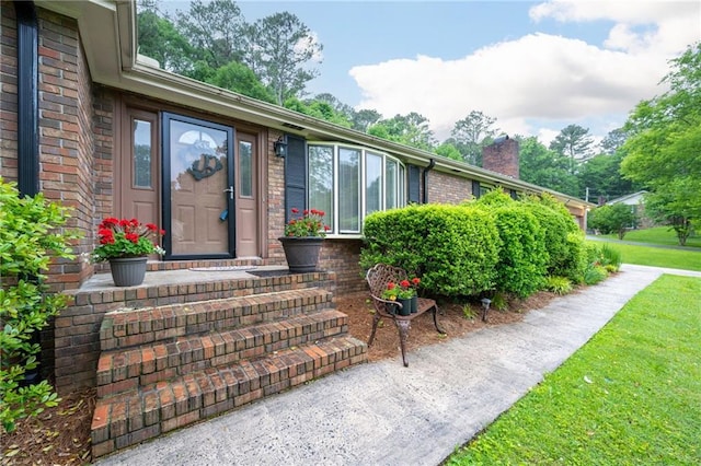 view of exterior entry featuring brick siding, a lawn, and a chimney