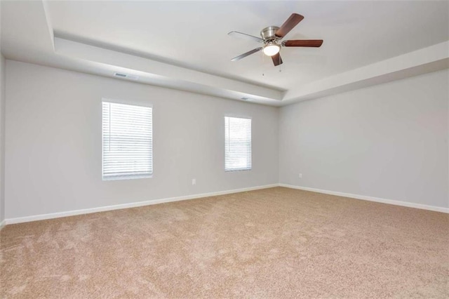 carpeted spare room with a raised ceiling and ceiling fan