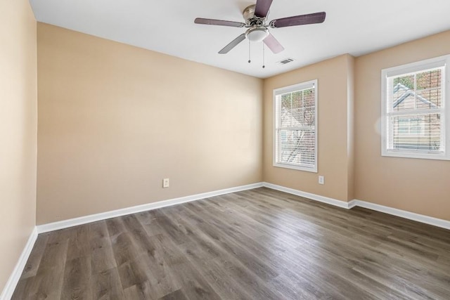 unfurnished room with dark wood finished floors, visible vents, a healthy amount of sunlight, and baseboards