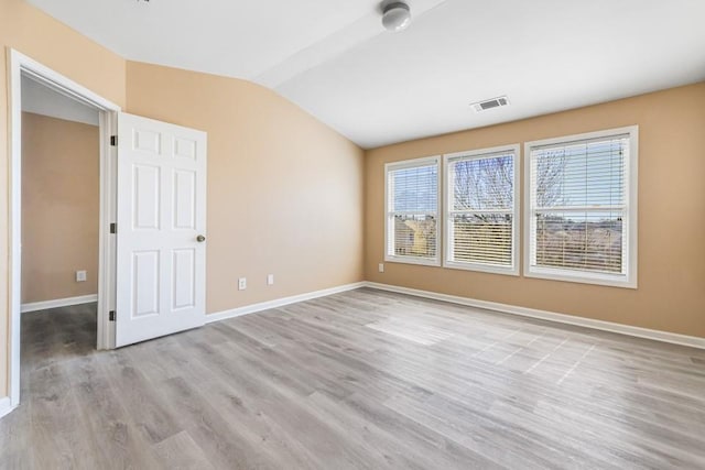 spare room with vaulted ceiling, light wood-style floors, visible vents, and baseboards