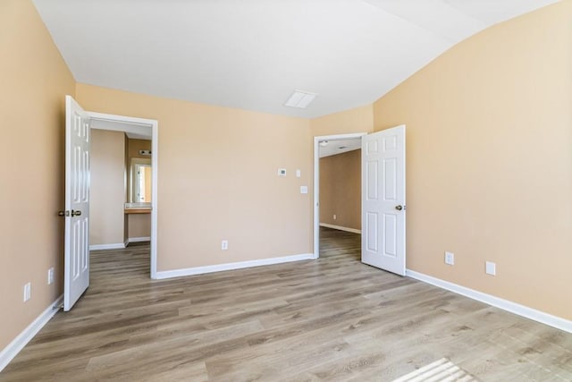 unfurnished bedroom featuring lofted ceiling, light wood-style floors, and baseboards