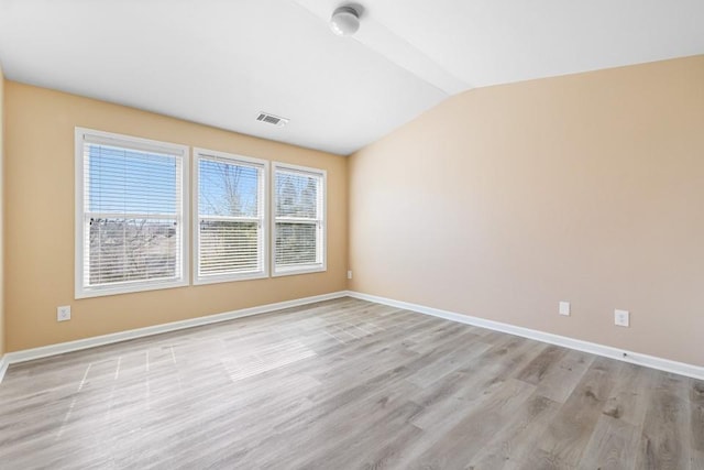 unfurnished room with light wood finished floors, visible vents, baseboards, and lofted ceiling