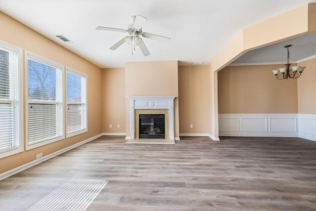 unfurnished living room with a glass covered fireplace, ceiling fan with notable chandelier, visible vents, and wood finished floors