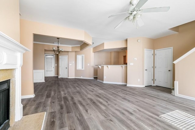 unfurnished living room featuring ceiling fan with notable chandelier, a fireplace, baseboards, and wood finished floors