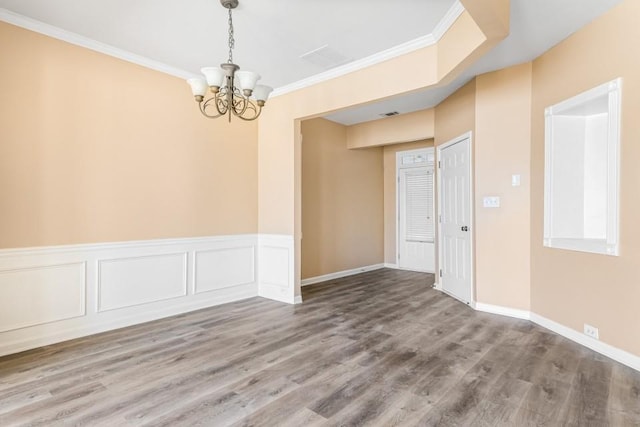 spare room featuring wainscoting, crown molding, an inviting chandelier, and wood finished floors