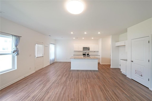 kitchen featuring wood-type flooring, stainless steel appliances, white cabinetry, and a kitchen island with sink