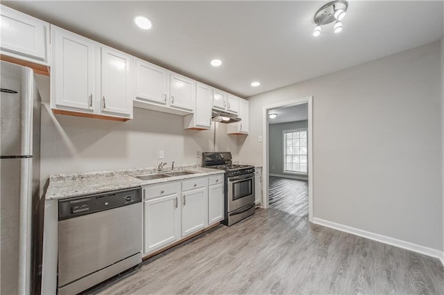 kitchen with light wood-type flooring, white cabinets, under cabinet range hood, appliances with stainless steel finishes, and a sink