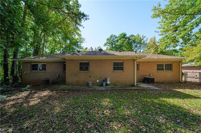 rear view of house with central AC, fence, brick siding, and a lawn