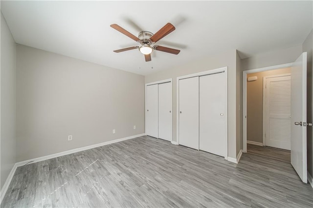 unfurnished bedroom featuring two closets, light wood finished floors, and baseboards