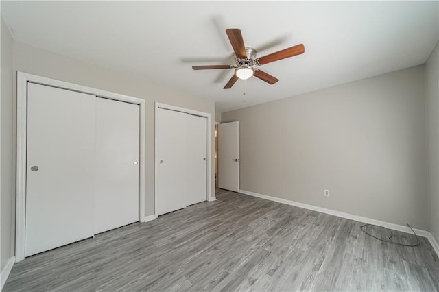 unfurnished bedroom featuring multiple closets, light wood finished floors, ceiling fan, and baseboards