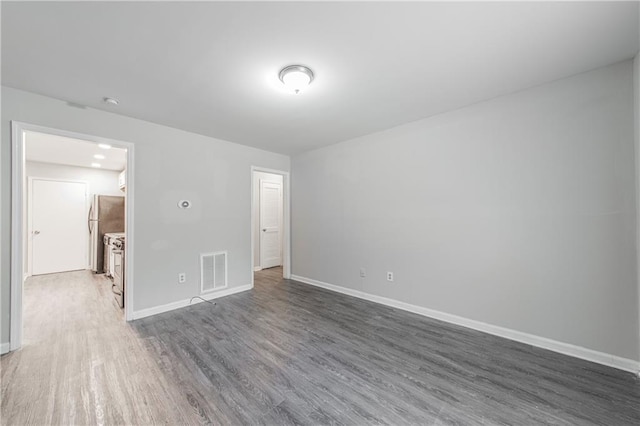 unfurnished bedroom featuring visible vents, baseboards, freestanding refrigerator, and wood finished floors