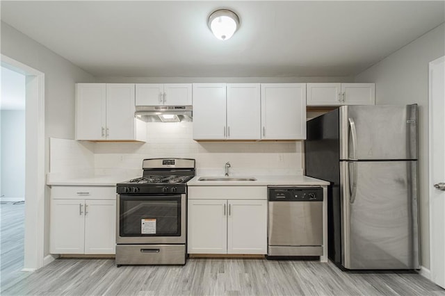 kitchen with a sink, light countertops, light wood-type flooring, under cabinet range hood, and stainless steel appliances