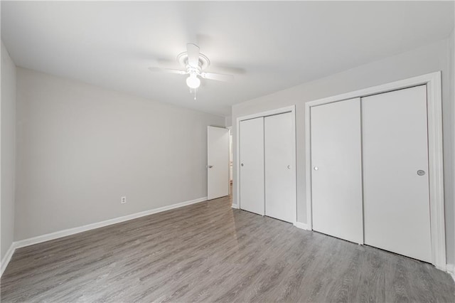 unfurnished bedroom with ceiling fan, baseboards, two closets, and wood finished floors