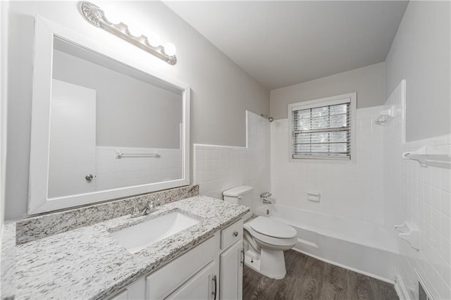 full bath with vanity, toilet, wood finished floors, washtub / shower combination, and tile walls