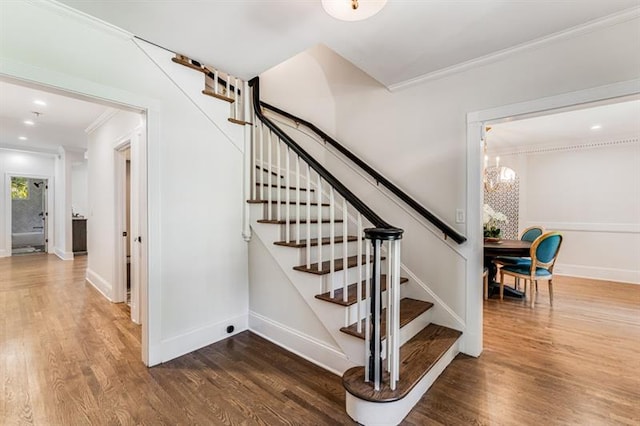 staircase with crown molding, hardwood / wood-style floors, and a chandelier