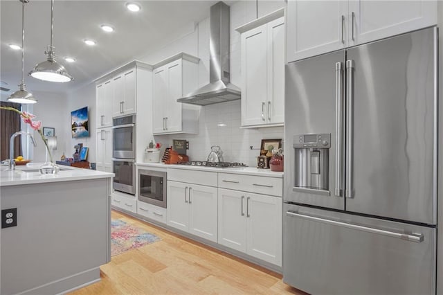 kitchen with appliances with stainless steel finishes, sink, wall chimney range hood, and white cabinets