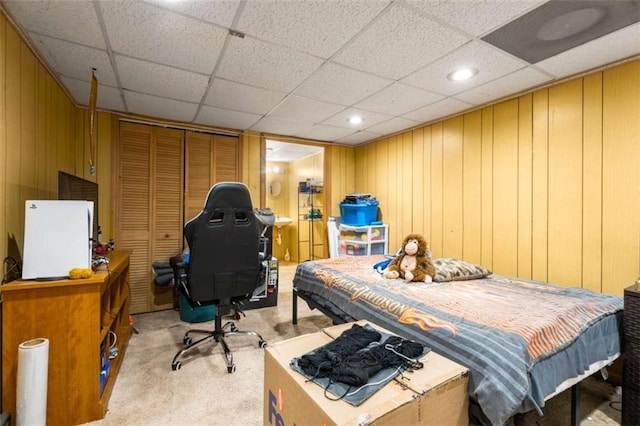 bedroom with a closet, a paneled ceiling, light colored carpet, and wooden walls