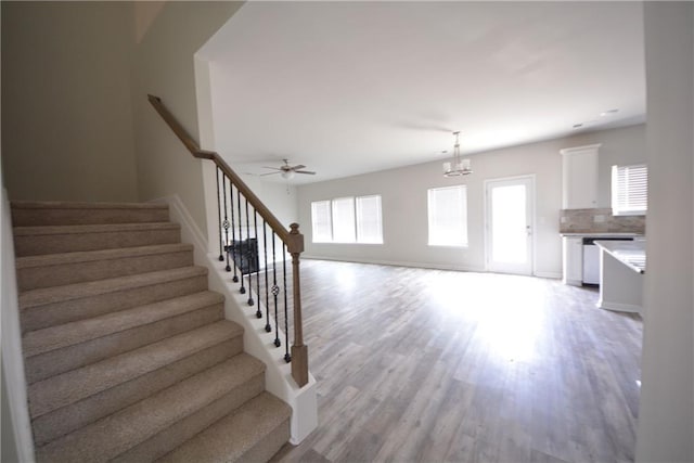 stairs with ceiling fan with notable chandelier, wood finished floors, and baseboards