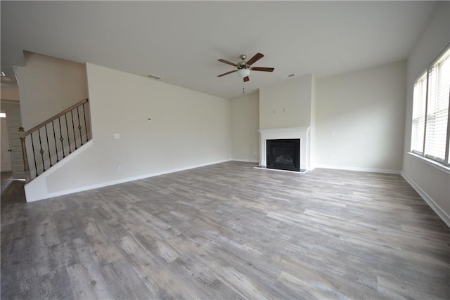 unfurnished living room featuring a fireplace with raised hearth, stairs, baseboards, and wood finished floors