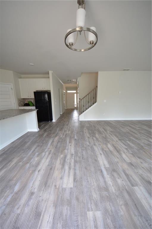 unfurnished living room with visible vents, stairway, baseboards, and light wood-type flooring