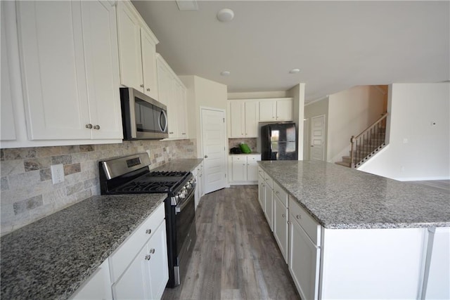 kitchen featuring wood finished floors, a center island, stainless steel appliances, white cabinets, and decorative backsplash