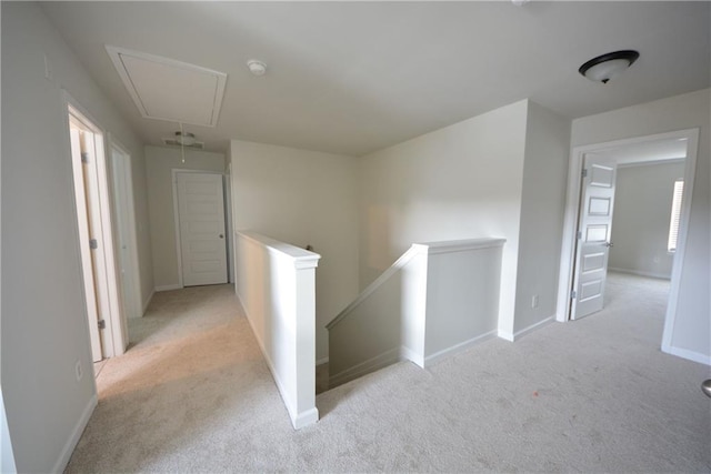 hallway with an upstairs landing, light carpet, attic access, and baseboards