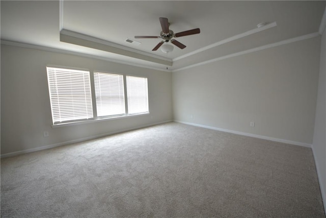 carpeted empty room with visible vents, ornamental molding, a ceiling fan, a tray ceiling, and baseboards