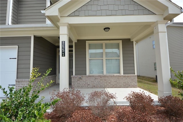 view of exterior entry featuring a garage, brick siding, and covered porch