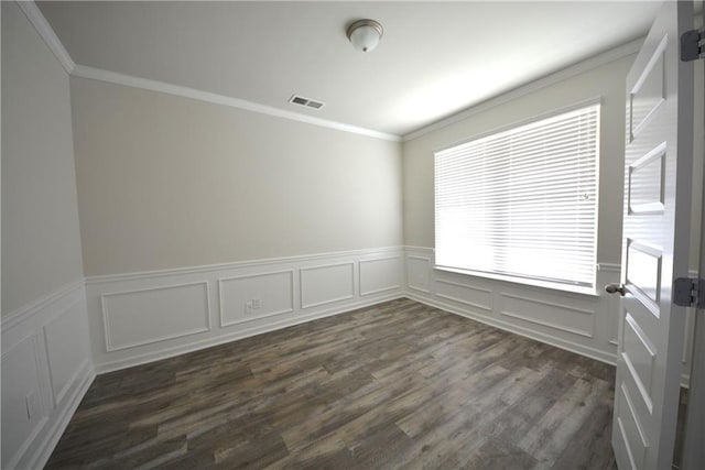 empty room with visible vents, crown molding, dark wood-type flooring, and a wainscoted wall